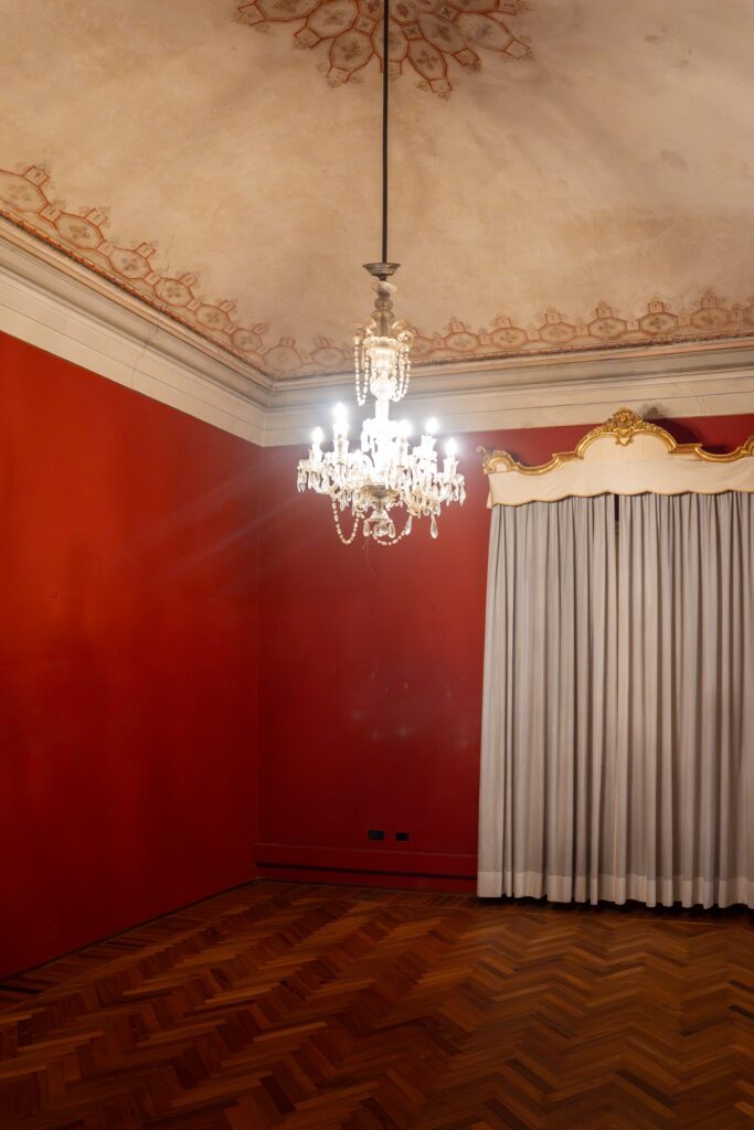 Sala rossa di Palazzo Le Stanze a Pistoia con soffitto decorato e lampadario.
