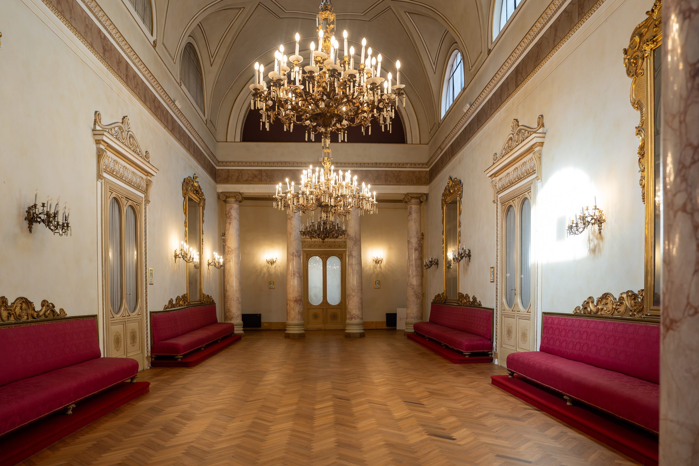 Il salone di Palazzo Le Stanze a Pistoia con lampadari, divani rossi e soffitto a volta.