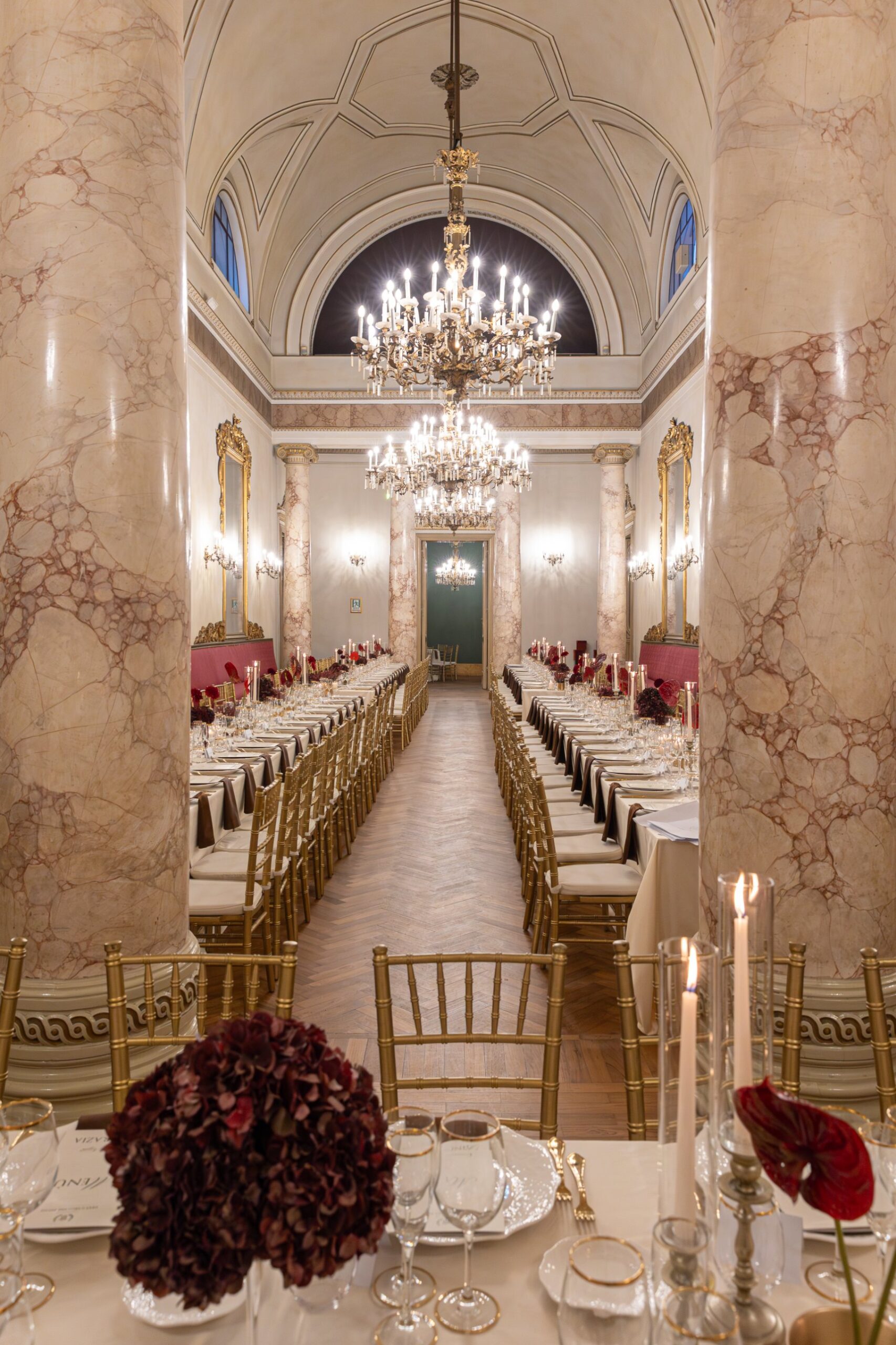 Il salone di Palazzo Le Stanze a Pistoia in prospettiva, con lampadari, colonne in marmo e lunga tavolata allestita per un evento.
